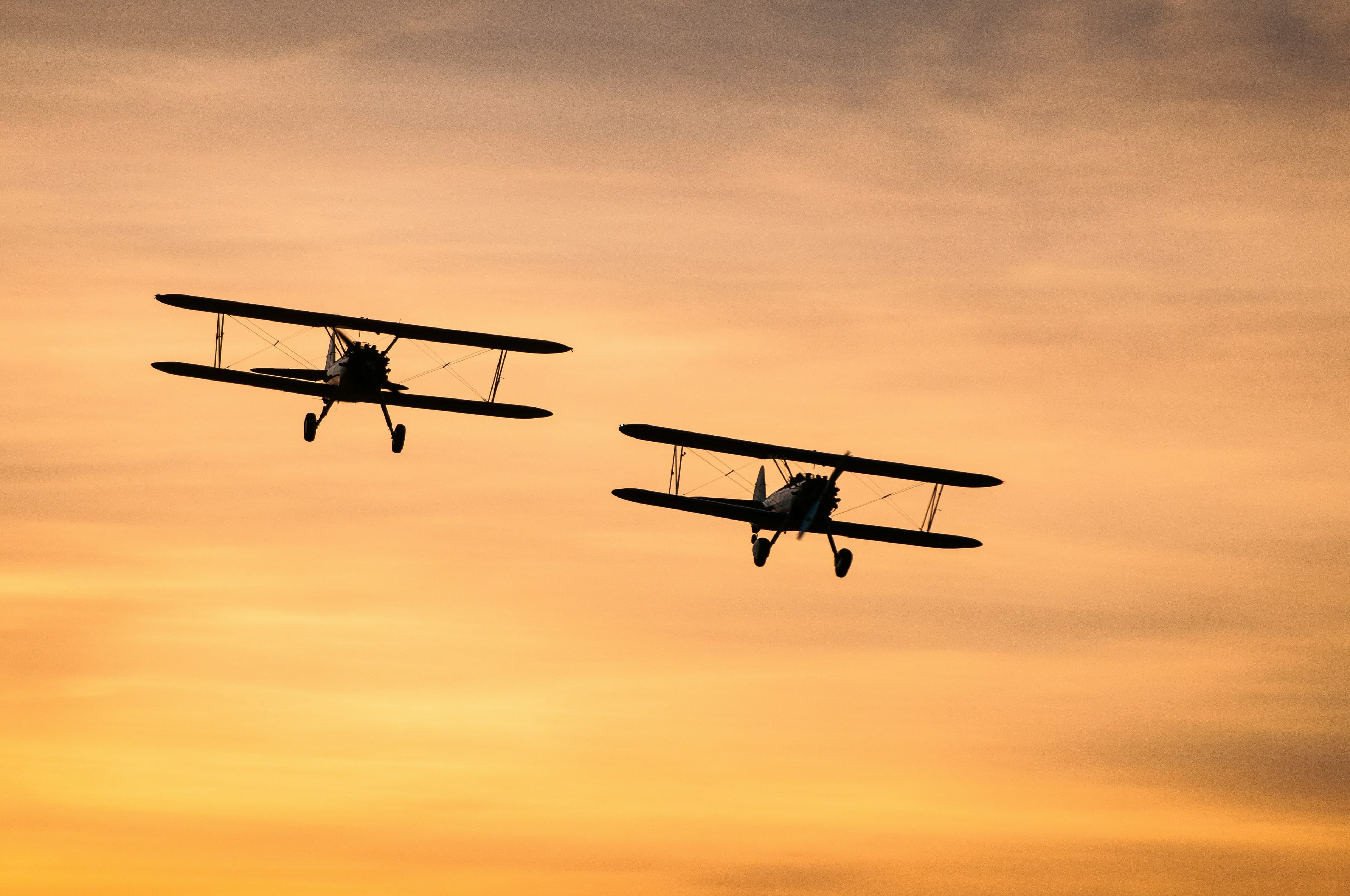 Two biplanes in formation flight against a sunset sky
